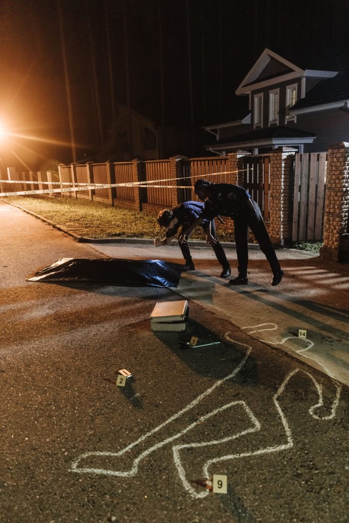 Polizeibeamte untersuchen nachts einen Tatort mit Beweismittelmarkierungen und einer Kreideumrisslinie.