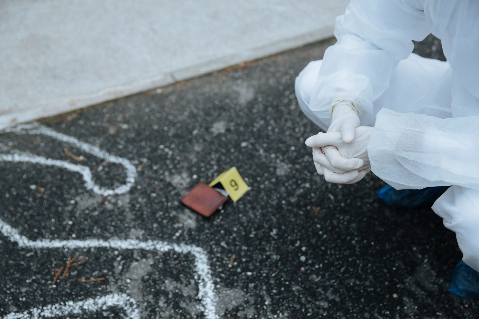 Ein Forensiker in Schutzanzug untersucht den auf dem Asphalt markierten Umriss des Tatorts.