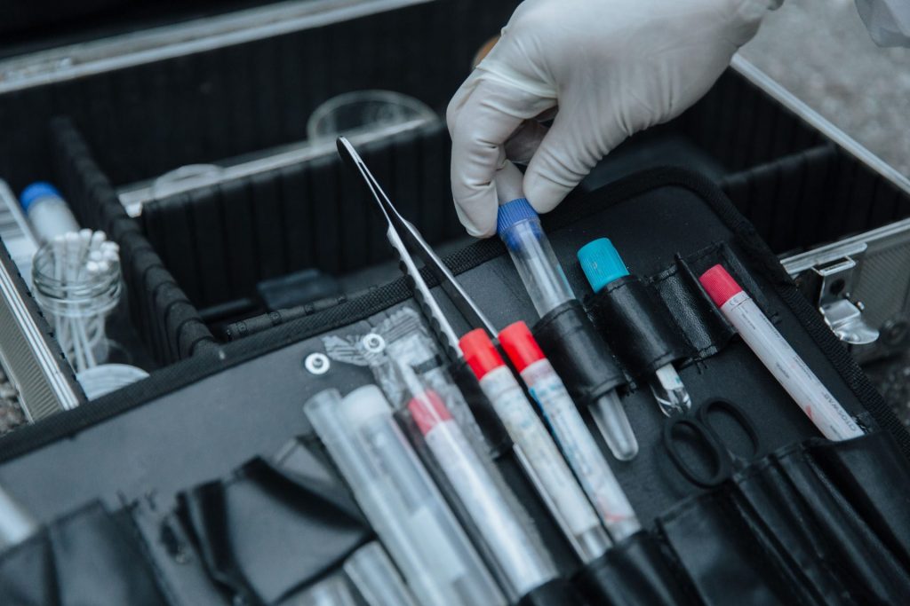 Mit Handschuhen bekleidete Hand hantiert mit einem Reagenzglas in einem Koffer mit forensischer Ausrüstung am Tatort.