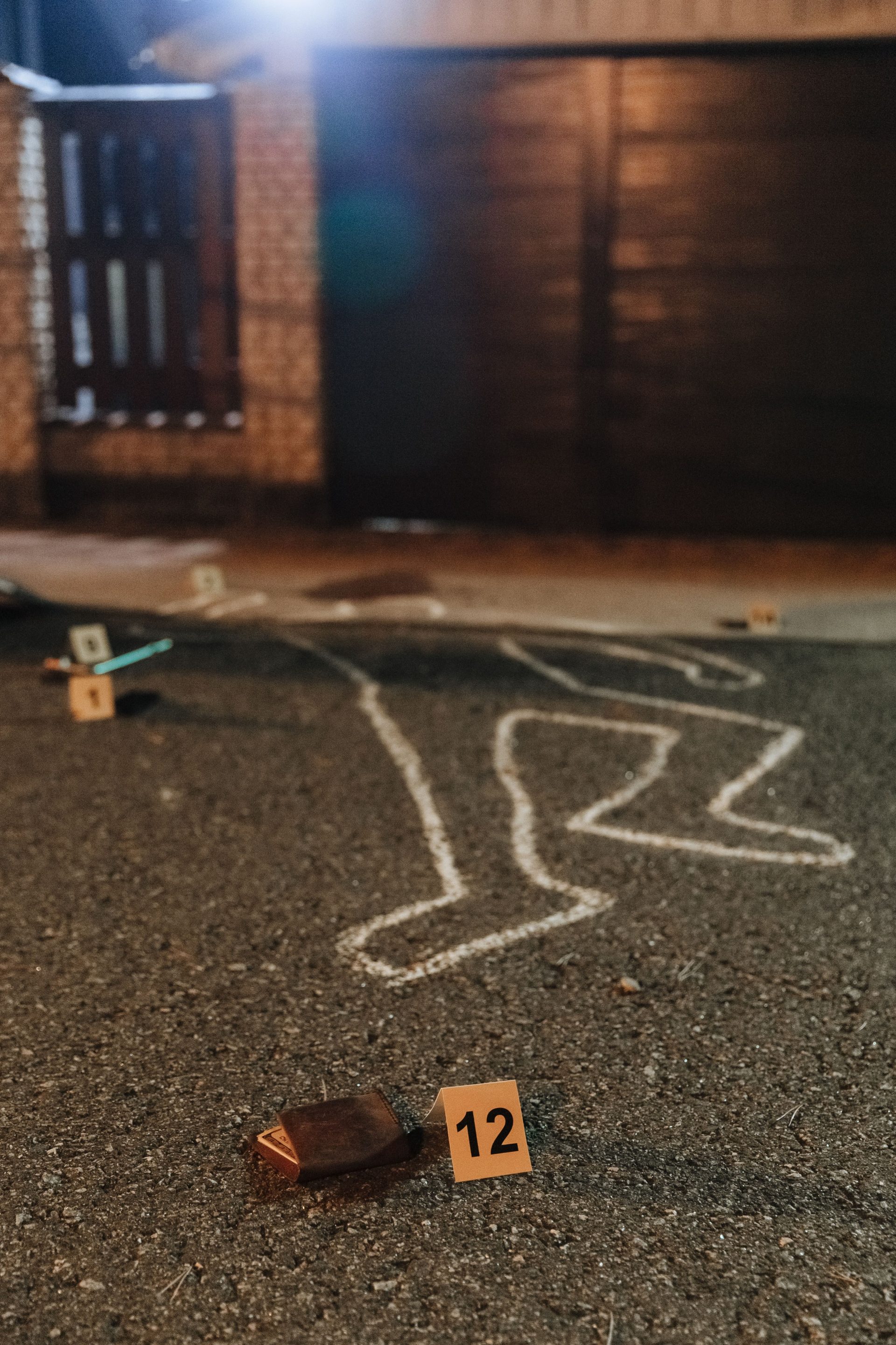 Kreideumriss und Beweismittelmarkierungen an einem Tatort im Freien bei Nacht.